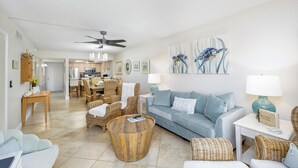 A living room with a sofa, wicker chairs, a coffee table, and a dining area with a table and chairs. - Sanibel Siesta on the Beach unit 607 (Sanibel)