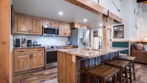 A kitchen with wooden cabinets, stainless steel appliances, a marble countertop, and a wooden island with stools.