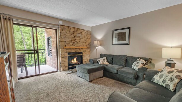 A living room with a stone fireplace, a grey sofa set, and a sliding glass door leading to an outdoor area. - two bedroom condo sleeps 6 persons (Gatlinburg)
