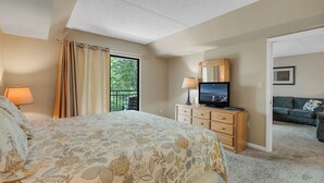 A bedroom with a large bed, a TV, a dresser, and a balcony with curtains. - two bedroom condo sleeps 6 persons (Gatlinburg)