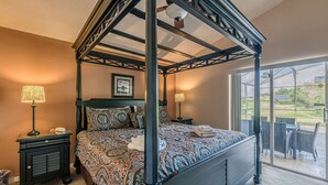 A four-poster bed with a patterned bedspread, bedside lamps, and a view of the outdoors through a glass door. - Luxury Pool Home, 2 Master Suites, Lakeview & Games Room. Disney 3 Miles (Kissimmee)