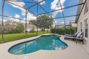 A swimming pool with a glass enclosure, surrounded by a patio area with lounge chairs and a small table.