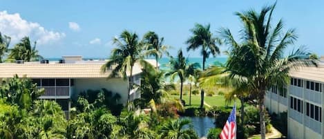 A resort with a swimming pool, palm trees, a view of the ocean, and an American flag.