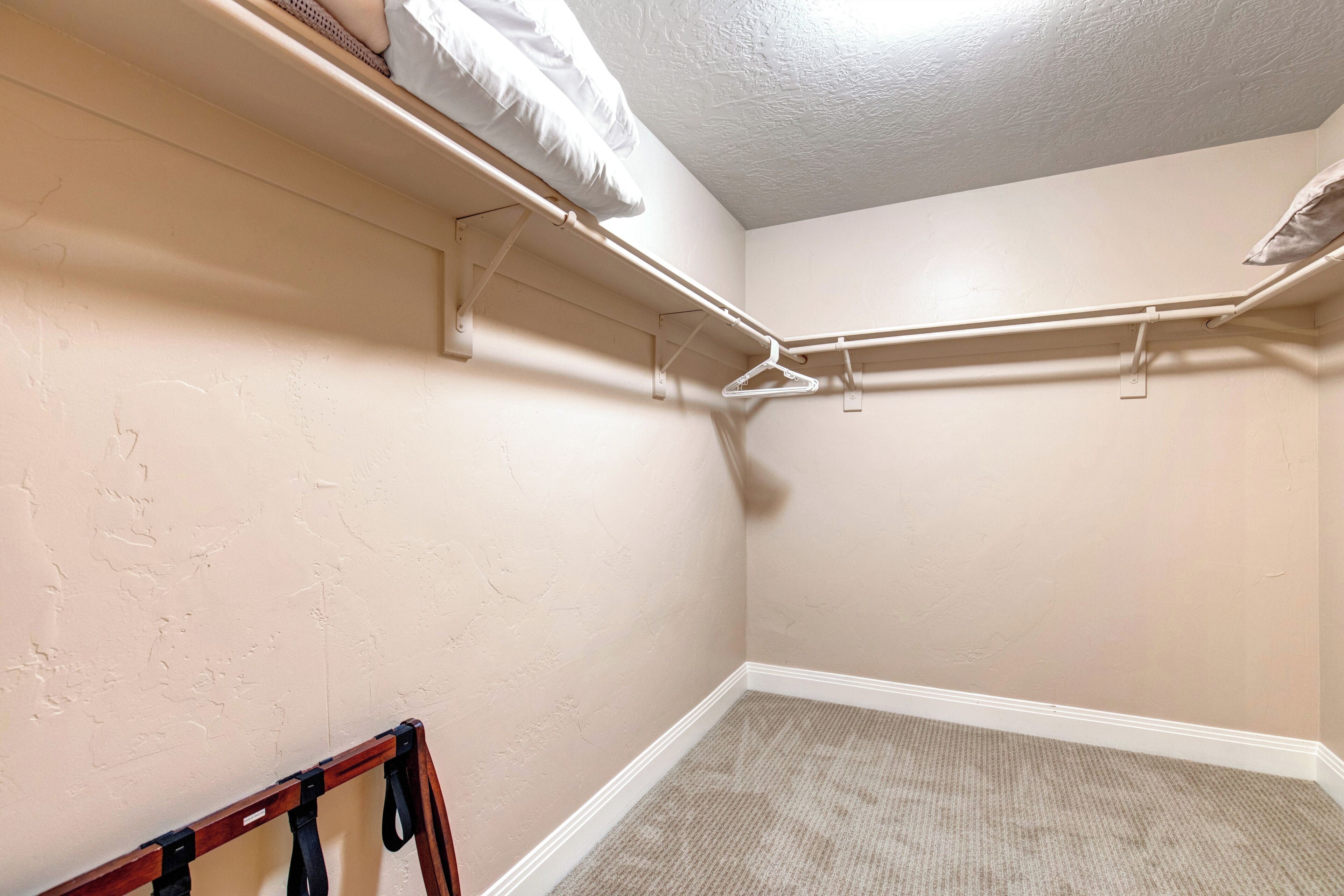 Una esquina de una habitación con paredes color beige, techo blanco y un perchero.