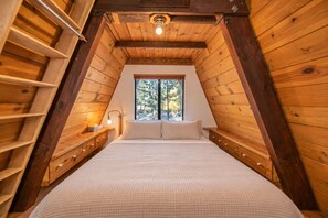 Une chambre avec un plafond en pente, des murs en bois, une fenêtre et un lit avec des oreillers.