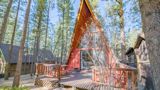 A cabin with a wooden deck, surrounded by tall pine trees. - A-Frame of Mind - Wood Stove Fireplace, Deck, Barbecue (Big Bear City)