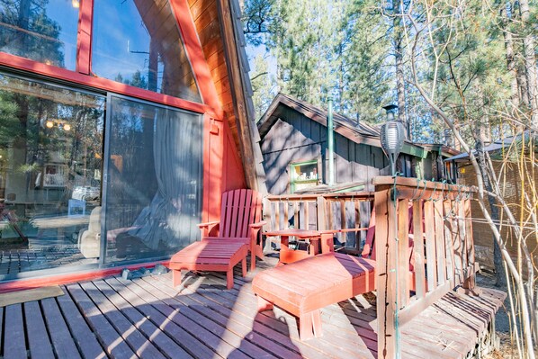 Une terrasse en bois avec des chaises rouges et une table, donnant sur une zone boisée.