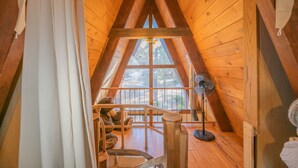 An attic room with wooden walls, a large window, a fan, and a teddy bear. - A-Frame of Mind - Wood Stove Fireplace, Deck, Barbecue (Big Bear City)