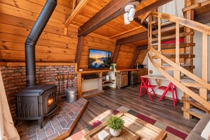 Interior acolhedor de uma cabana com lareira, escada de madeira e vista para o exterior.