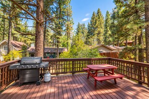 Une terrasse avec un barbecue, une table de pique-nique et des arbres tout autour.