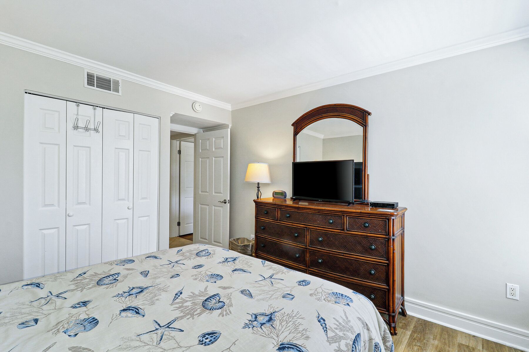 A bedroom with a bed, dresser, mirror, and white doors.