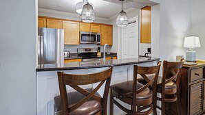 Una cocina moderna con electrodomésticos de acero inoxidable, armarios de madera y una isla central con taburetes de bar.