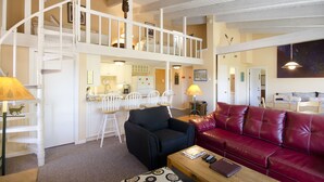 A spacious loft-style living area with a high ceiling, a staircase, a dining area, and a red leather couch. - SE076 | Mountainside Condo | View | Hot Tub | Winter Shuttle | Ski In/Out (Steamboat Springs)
