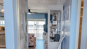 Un pasillo con una silla de mimbre blanca, una puerta que da a una habitación y un suelo de baldosas.