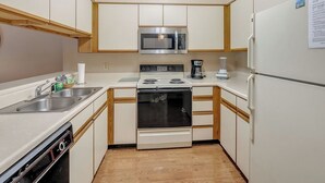 Une cuisine compacte avec des meubles blancs, un four à micro-ondes, une cuisinière, une machine à café et un réfrigérateur.
