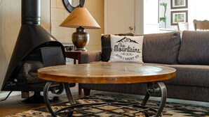 A cozy living room with a wood-burning stove, a round wooden table, a sofa with a mountain-themed pillow, and a mirror on the wall. - Walk from Park City Lifts to Heated Pool/Hot Tub Managed by Park City Lodging (Park City)