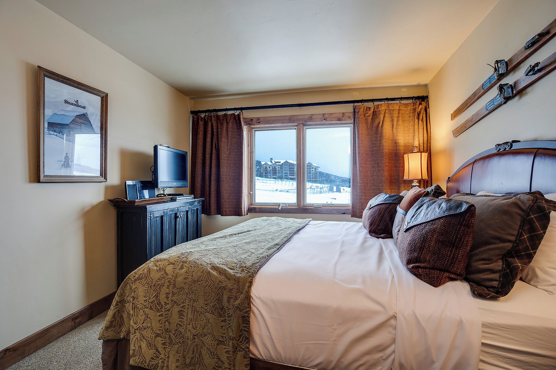A hotel room with a bed, a television, a window with curtains, and a view of a building outside.