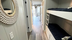 A narrow hallway with a mirror, a sign that says "Kick off your shoes," and bunk beds on one side. - Breathtaking Ocean Views, Steps to Coligny Plaza! (Hilton Head)