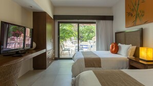 A hotel room with a TV on a wooden desk, a bed with white and brown bedding, a nightstand with a lamp, and a sliding glass door leading to an outdoor area with a pool and chairs. - Completely Renovated with Private Pool WIFI (Playa del Carmen)