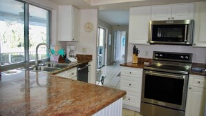 A modern kitchen with granite countertops, stainless steel appliances, and white cabinetry. - Now Available! Enjoy Panoramic Water Views, Pool, Dock, Beach Parking Permit & Pup Friendly! (Sanibel)