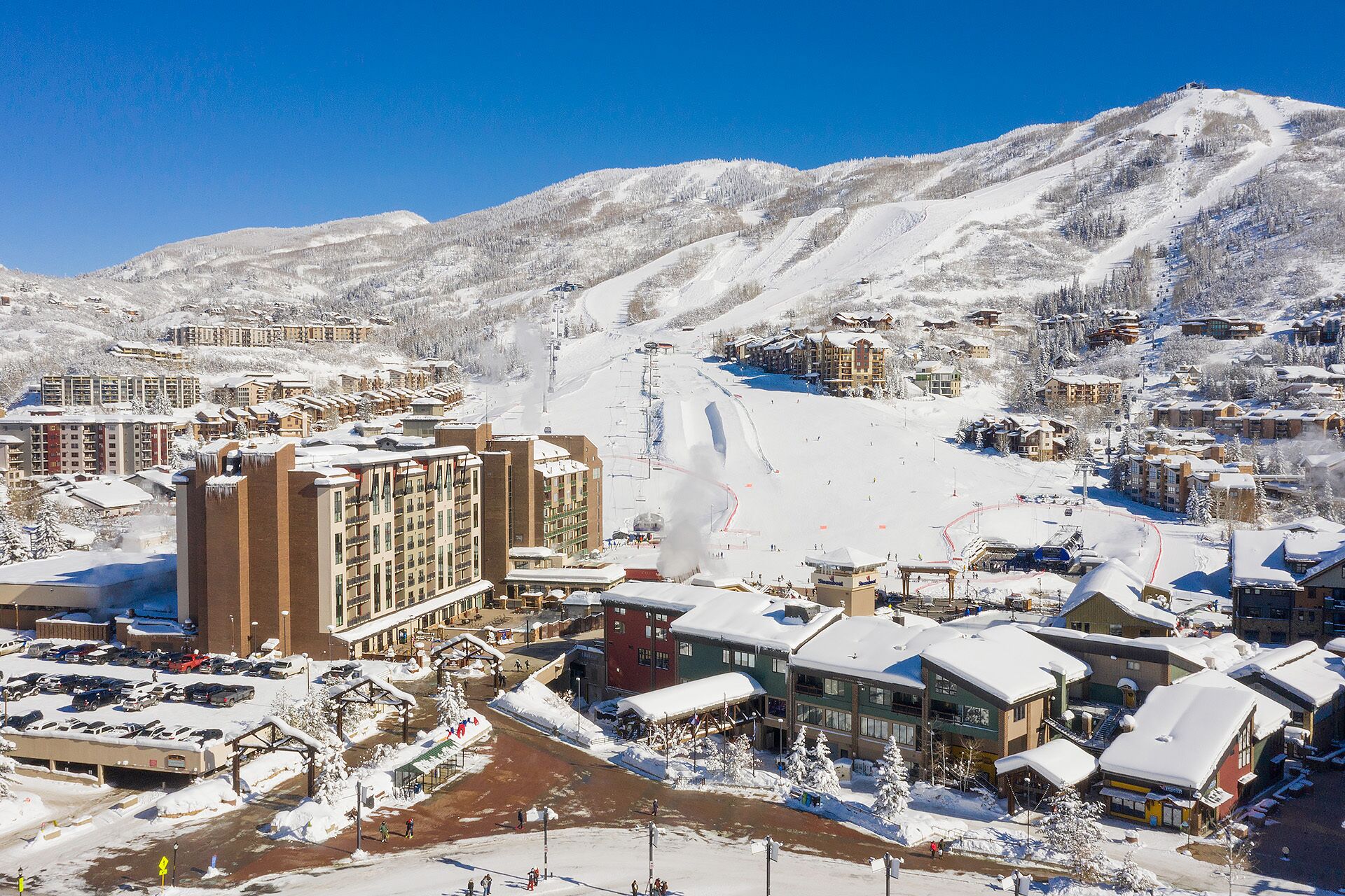 Un centro de esquí cubierto de nieve con varios edificios, incluyendo un hotel grande de varios pisos y un telesilla visible al fondo.