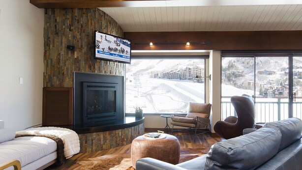 A cozy living room with a fireplace, leather sofas, a flat-screen TV, and a view of a snowy landscape.