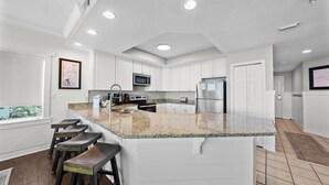 Una cocina moderna con armarios blancos, encimera de granito y una isla integrada con taburetes de bar.