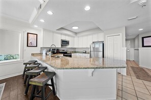 Una cocina moderna con armarios blancos, encimera de granito y una isla integrada con taburetes de bar.