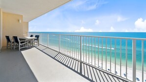 Un balcón con vistas al océano y la playa, con una mesa y sillas.