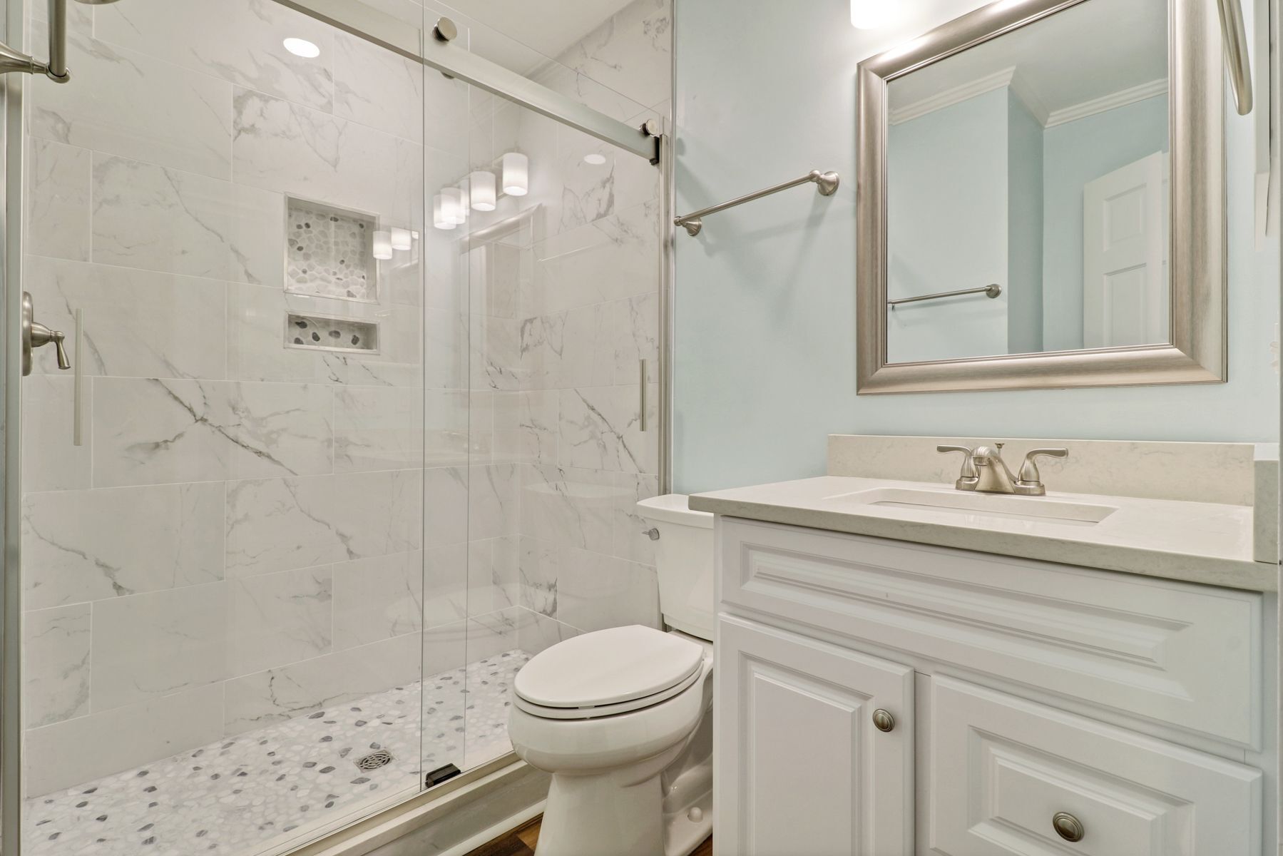 A bathroom with a glass-enclosed shower, a toilet, and a vanity with a mirror.