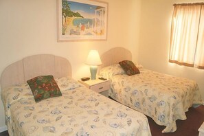 A room with two single beds, a nightstand with a lamp, a framed picture on the wall, and a window with curtains.