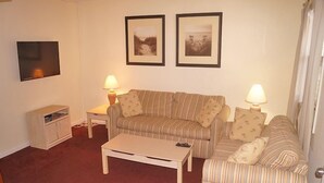 Una sala de estar con un sofá a rayas, dos lámparas, un televisor y un mueble bajo.