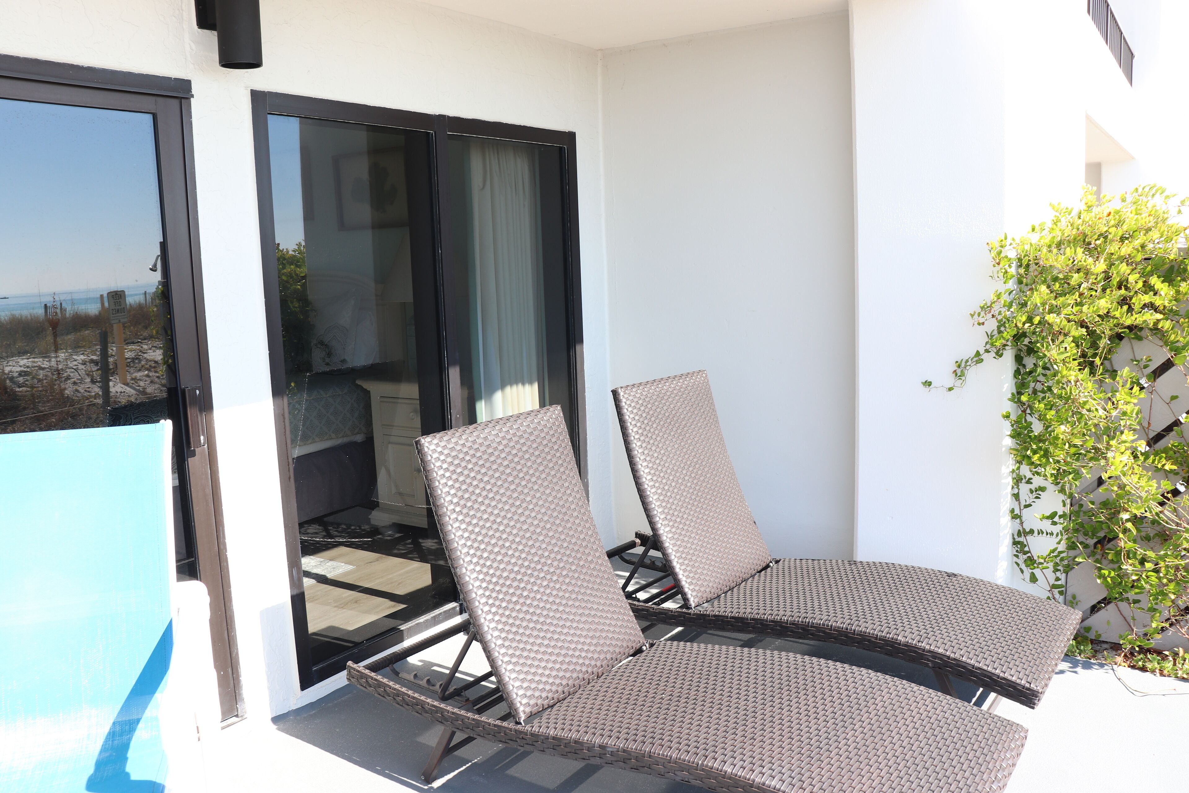 Un balcon avec deux fauteuils en osier et une porte vitrée donnant sur un espace piscine.