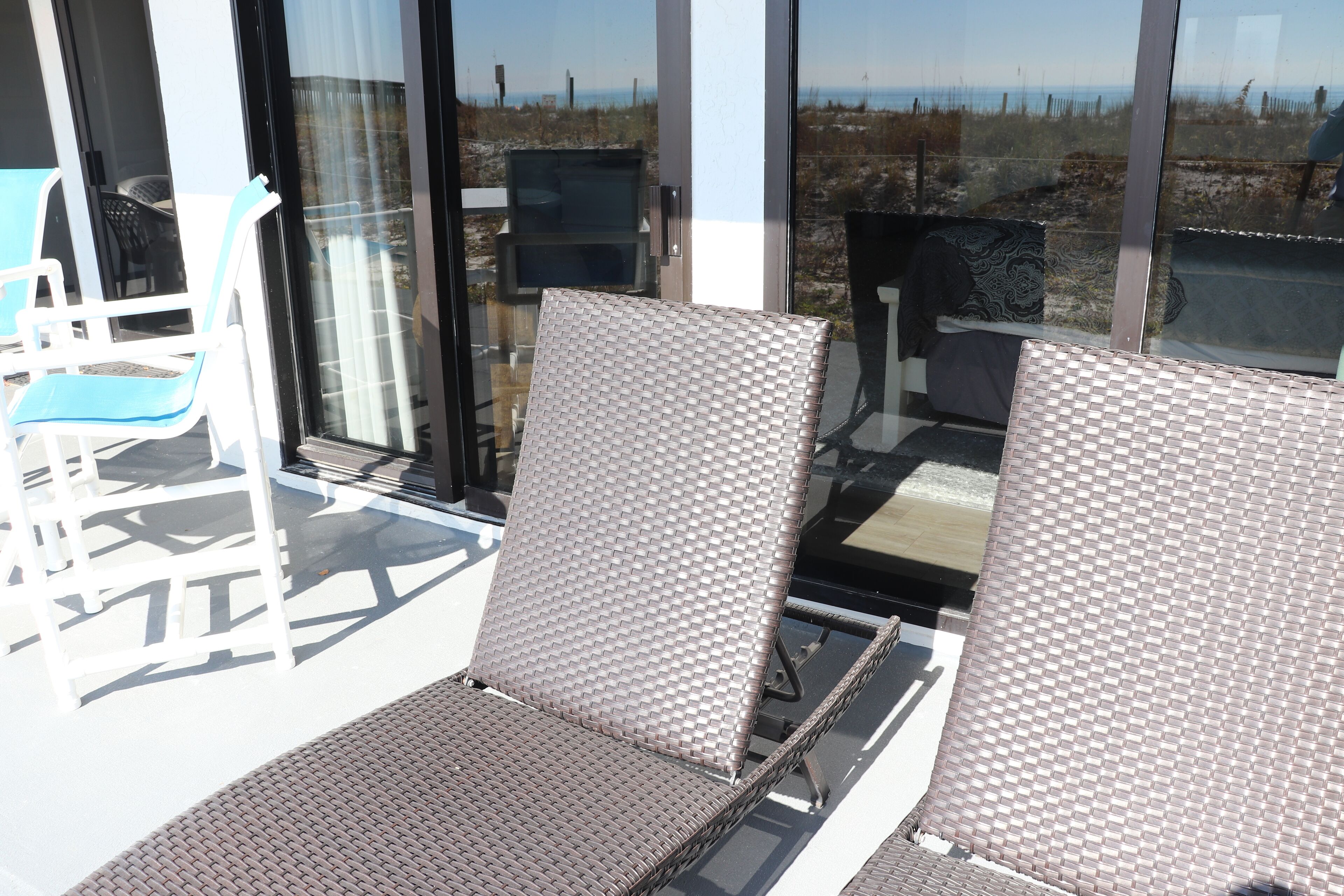 Ein Balkon mit zwei Korbstühlen, einem kleinen Tisch und einer Glastür mit Blick auf den Strand.