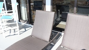 Ein Balkon mit zwei Korbstühlen, einem kleinen Tisch und einer Glastür mit Blick auf den Strand.