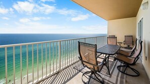 A balcony with a view of the ocean, a table with chairs, and a small screen. - Crystal Shores West 1107- Live the Beach Life! What are you Waiting For? (Gulf Shores)
