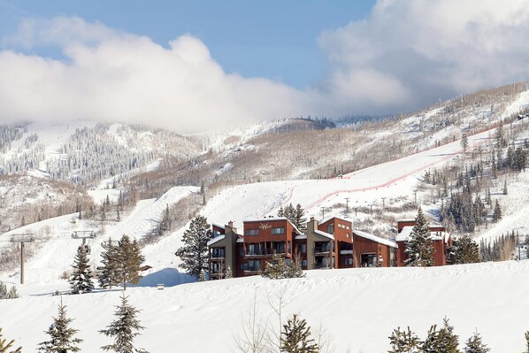 A ski resort with a building featuring multiple balconies and a ski slope in the background.