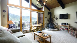 A cozy living room with a sofa, a coffee table, a fireplace, and a balcony with a view of the mountains. - W3537 | Exceptional View | Walk to Mtn Village | Pool | Hot Tub | Winter Shuttle (Steamboat Springs)