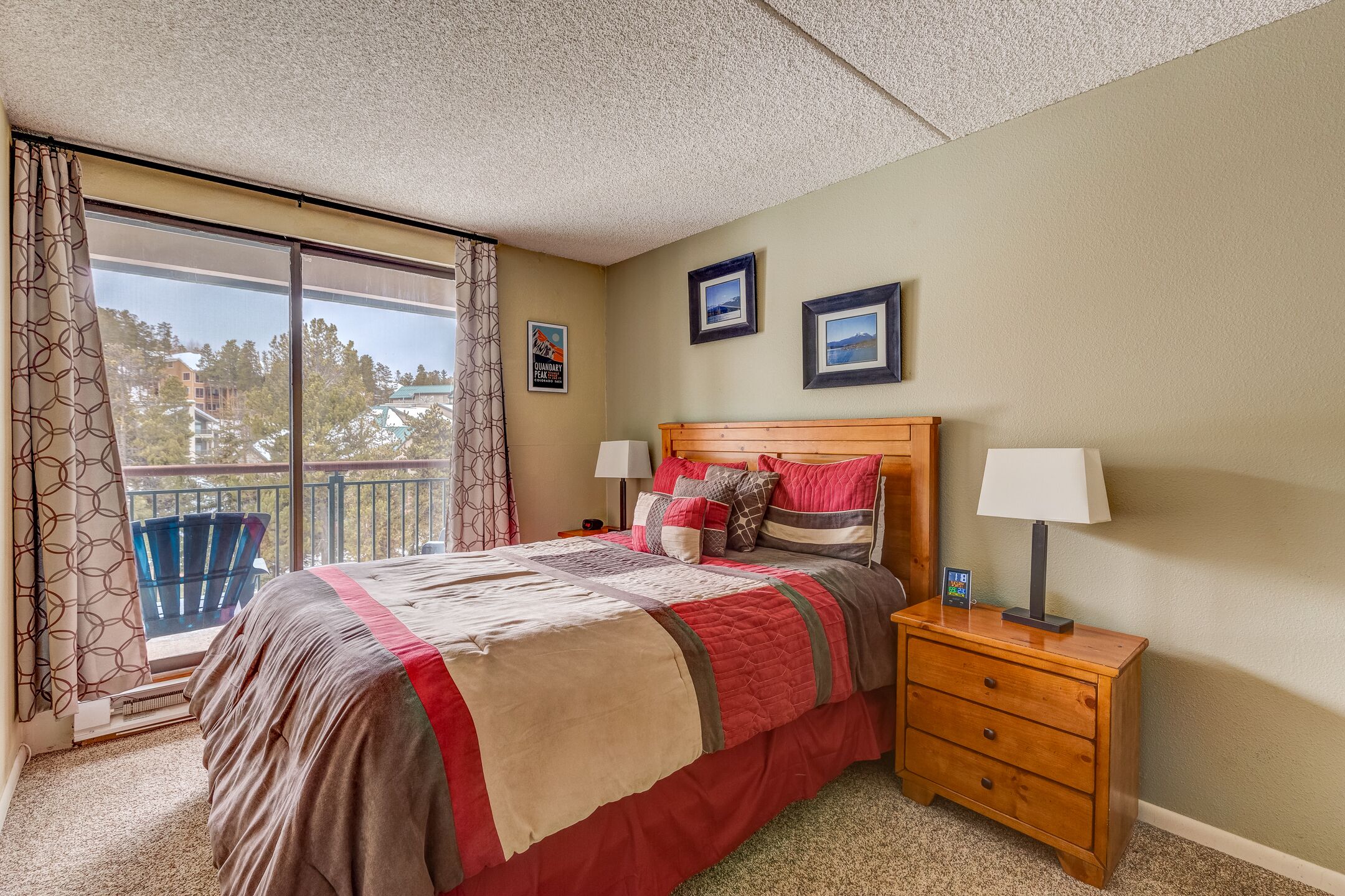 A bedroom with a large bed, a nightstand, a window with curtains, and a balcony.