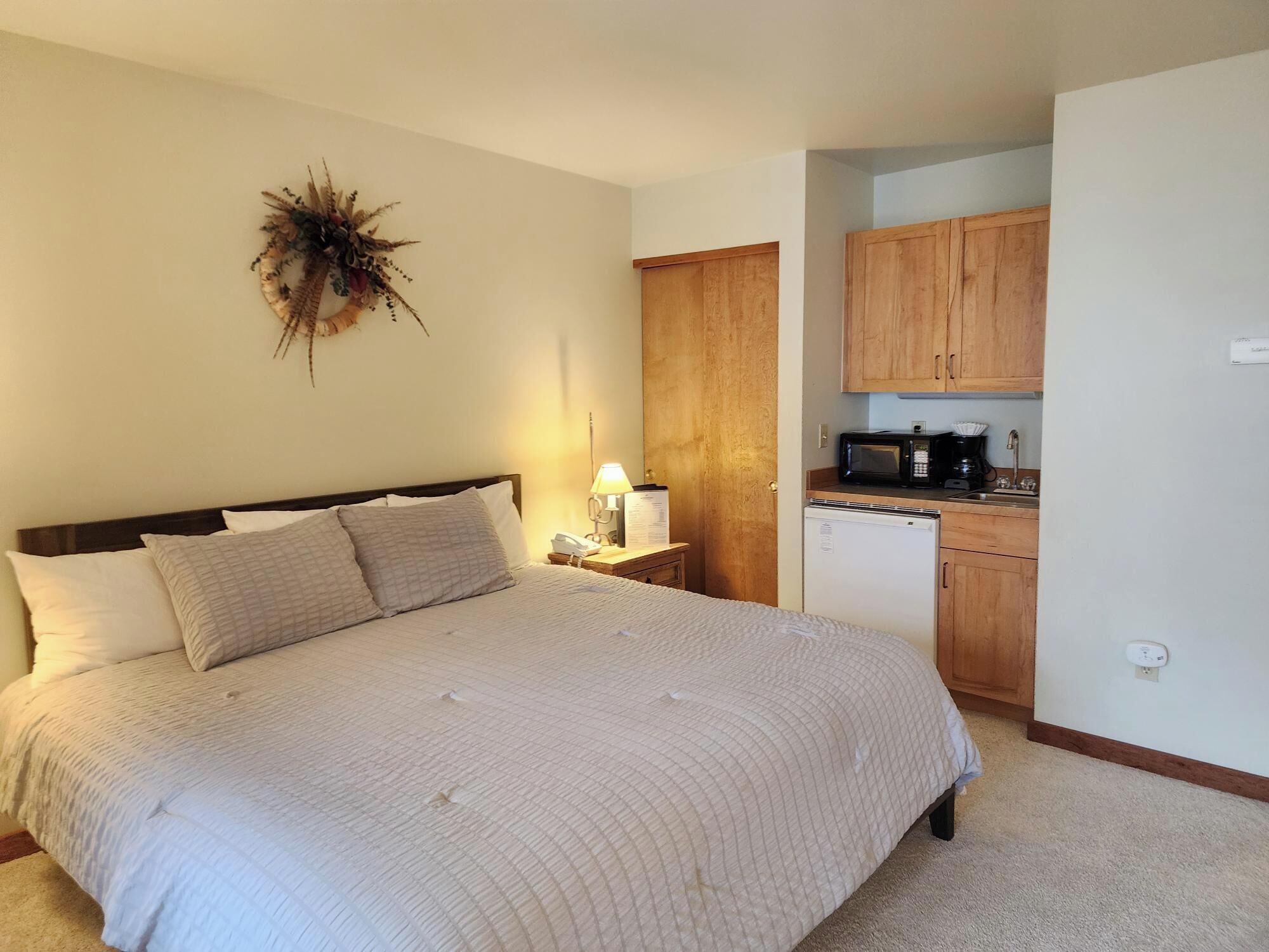 A bedroom with a bed, bedside lamp, and a small kitchenette with a microwave and refrigerator.