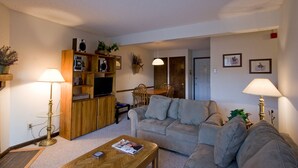 Una sala de estar con sofá, mesa de centro, mueble de entretenimiento de madera y dos lámparas.