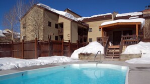Una piscina con cubierta de madera, rodeada de edificios nevados y una valla de madera.