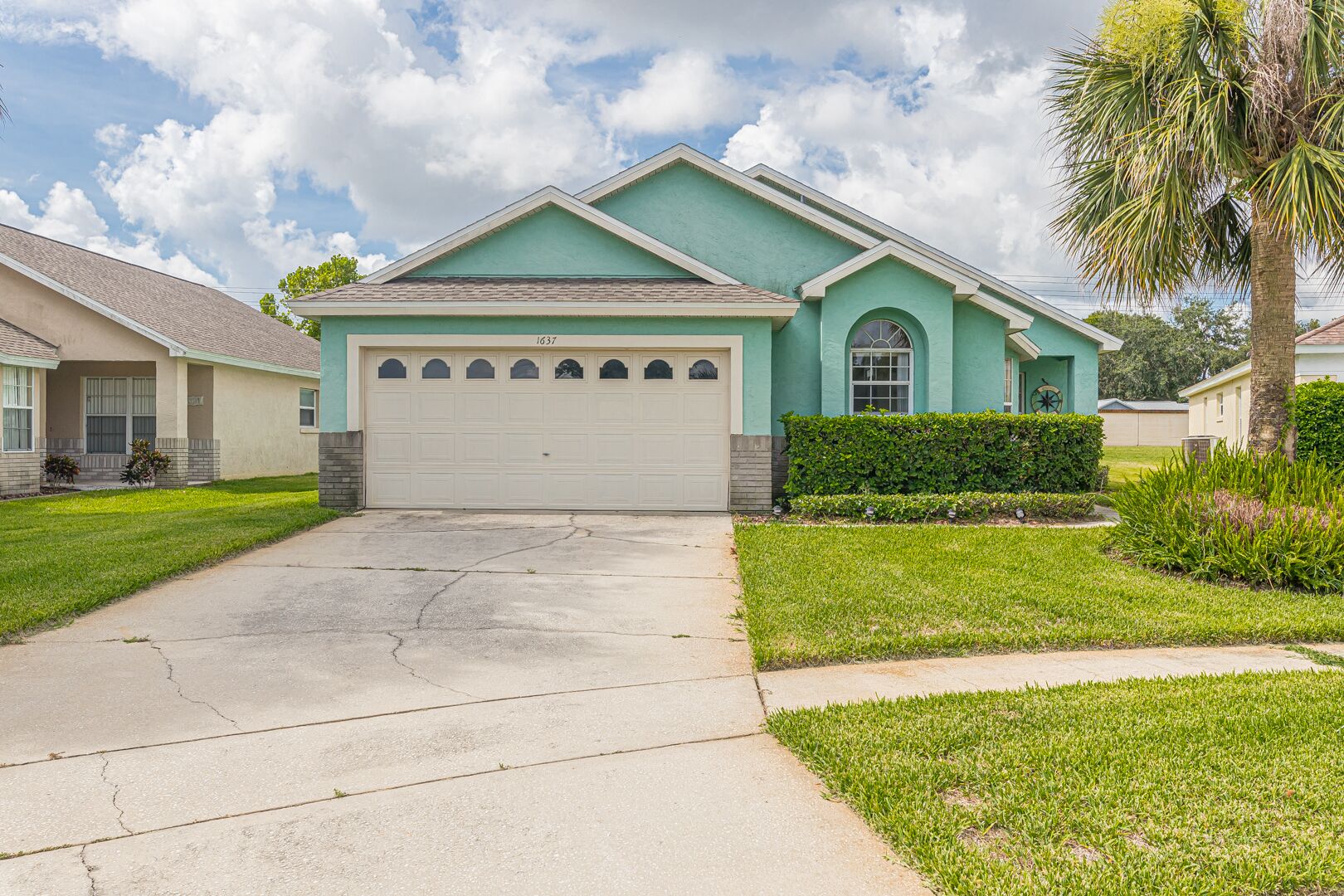 A single-story house with a garage, a well-maintained lawn, and a palm tree.