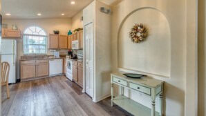 A kitchen with wooden cabinets, a microwave, a sink, and a stove. There is a small table with a bowl on it and a decorative wreath on the wall.