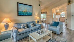 A living room with a sofa, coffee table, and lamps. There is a painting of a sailboat on the wall.