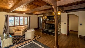 A spacious living room with a fireplace, wooden ceiling beams, and a large window with curtains. - Breathtaking Mt Washington Views  Jackson Chalet (Jackson)