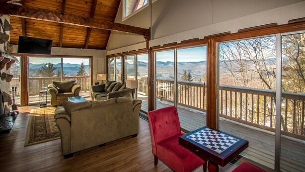 A spacious living room with a large window overlooking a scenic mountain view, furnished with a sofa, chairs, and a chess table. - Breathtaking Mt Washington Views  Jackson Chalet (Jackson)
