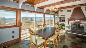 A dining area with a wooden table and chairs, a fireplace, and large windows offering mountain views. - Breathtaking Mt Washington Views  Jackson Chalet (Jackson)
