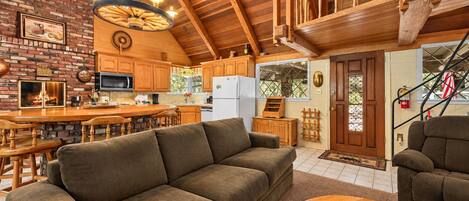 A cozy interior with a wooden ceiling, a fireplace, a kitchen with wooden cabinets, and a seating area with a sofa and a coffee table.