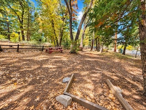 A campsite with picnic tables, a fire pit, and a natural forest setting.
